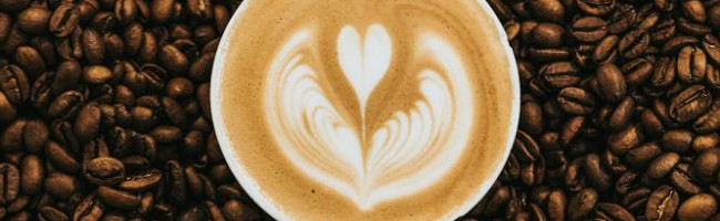 A coffee cup in a sea of beans. The latte art is a small heart inside a broken heart