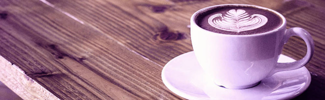 A cup of coffee sits upon a wooden table, lovely latte art drawn with foam.