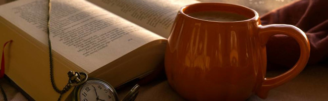 An orange coffee mug lies next to an open book and a pocketwatch.