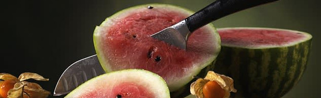 A knife is stabbed through one half of a watermelon.
