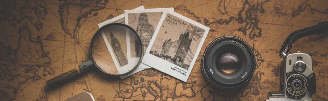A magnifying glass, three polaroids, a camera lense and part of a camera is seen sitting on top of an old-timey map.